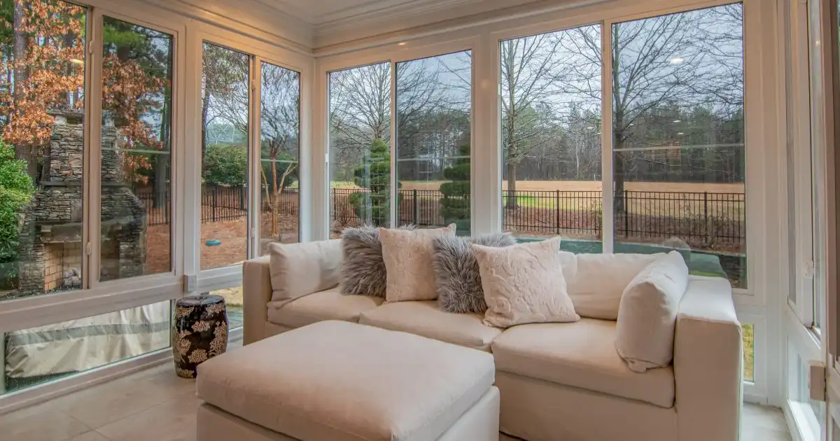 White sofa in sunroom with large windows.